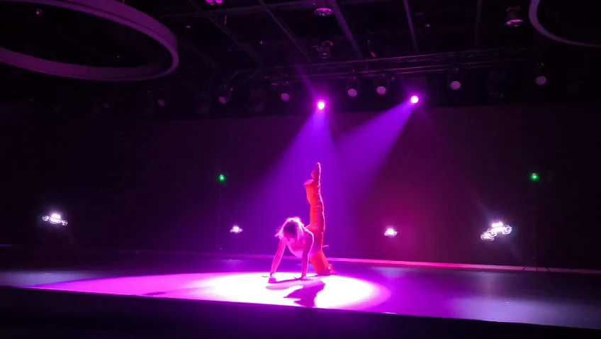 Tanečnica pod fialovými reflektormi počas indoor dronovej show